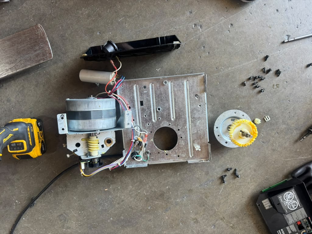 Disassembled garage door opener motor, gears and capacitor laid out on the floor during a repair