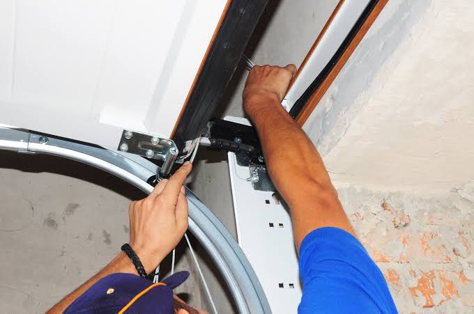 Technician repairing a garage door lifting cable along the track