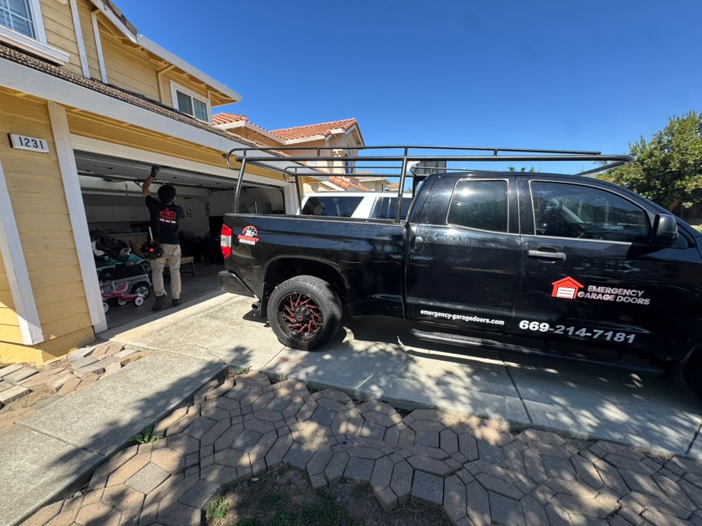 Emergency Garage Doors technician working on an open garage door beside the branded service truck in a residential driveway
