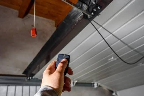 Technician testing a garage door remote aimed at the opener rail and emergency release
