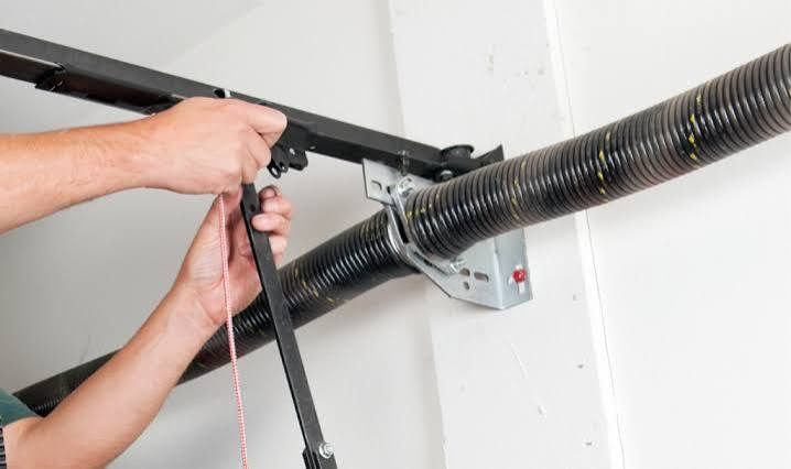 Technician securing the opener arm and red emergency release cord beside the torsion spring
