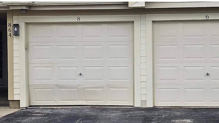 Two white sectional garage doors with a dented and buckled bottom panel needing panel replacement
