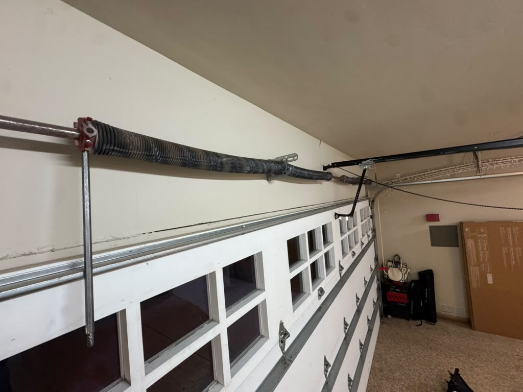 Torsion spring lifting system and opener rail above a white paneled garage door inside a home