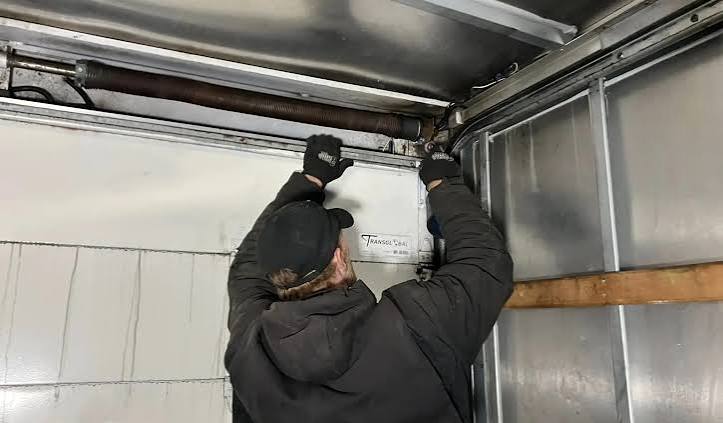 Technician adjusting a garage door torsion spring above the door header