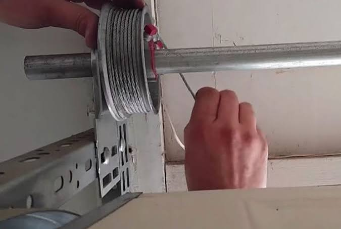 Technician re-spooling a garage door cable back onto the drum grooves