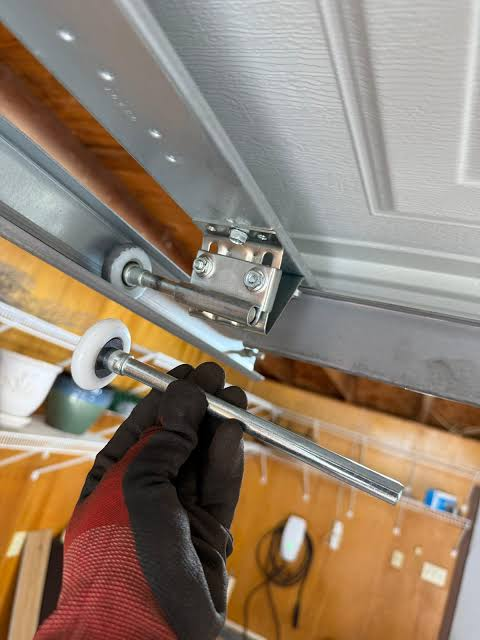Gloved hand holding a new nylon garage door roller beside the track