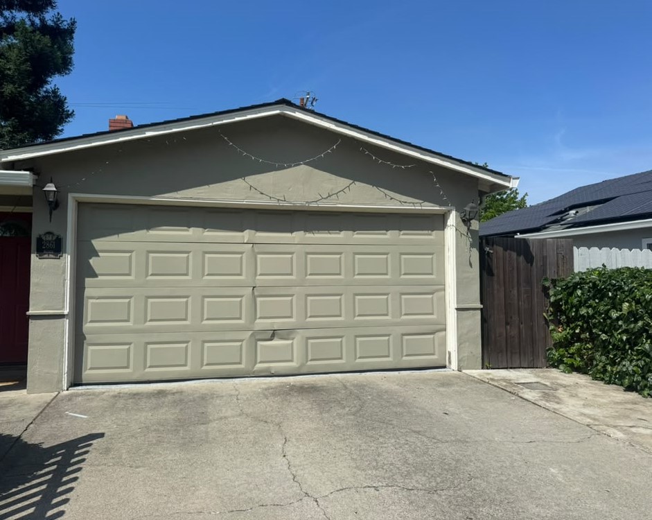 Beige double garage door with a cracked and split panel on a Salinas home before repair