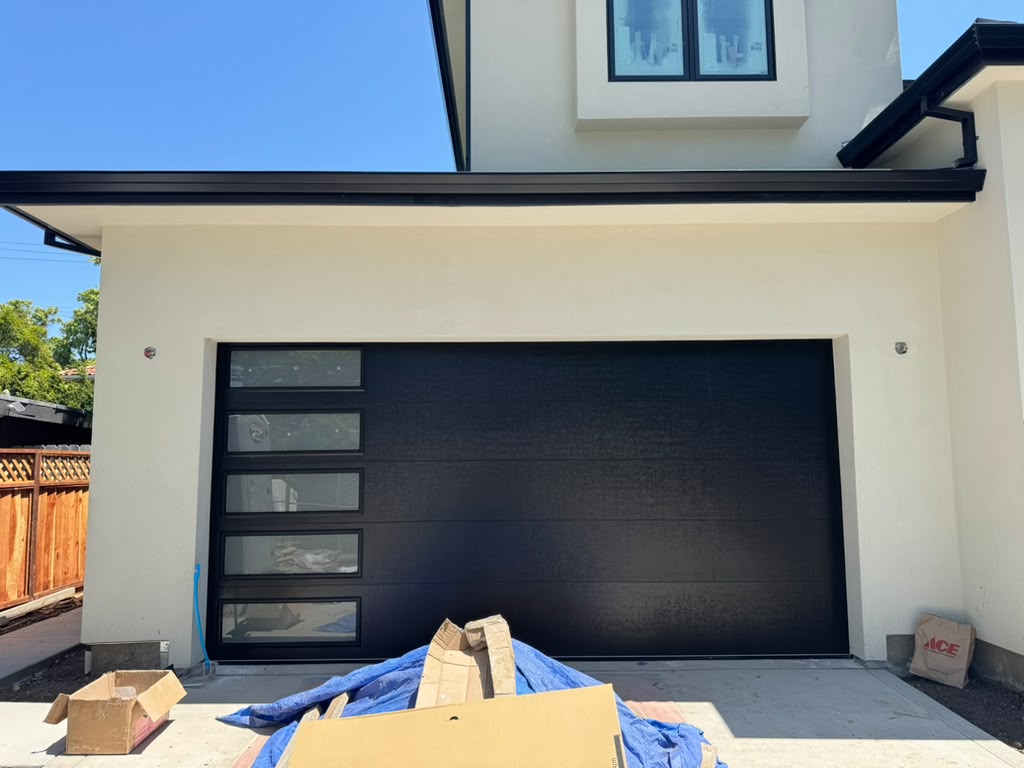 New modern black garage door with glass window inserts installed on a Monterey County home
